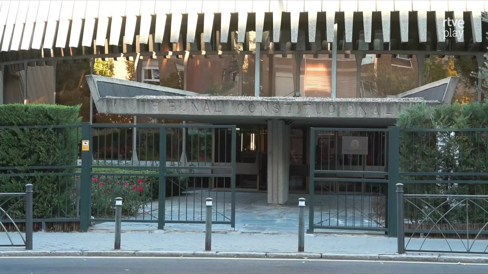 Entrada principal del Tribunal Constitucional de España en Madrid, con una marquesina de hormigón, valla metálica verde y acera peatonal.