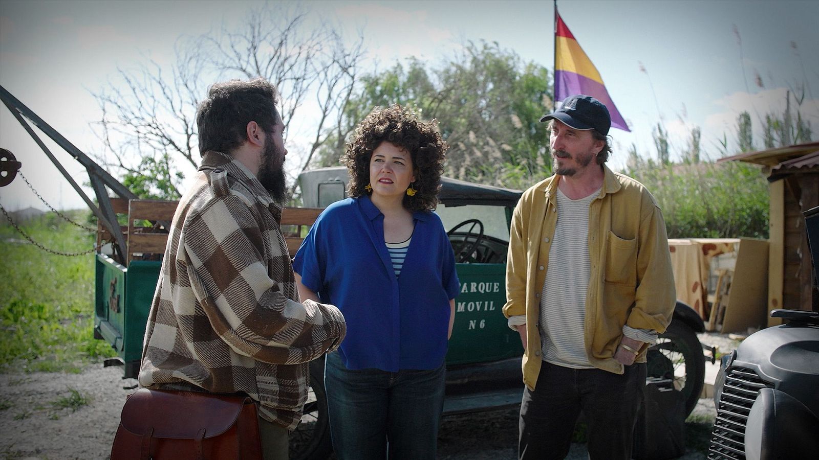 Tres personas conversan en un rodaje rural junto a un camión militar histórico rotulado y la bandera republicana, con Eloi Vila a la derecha.