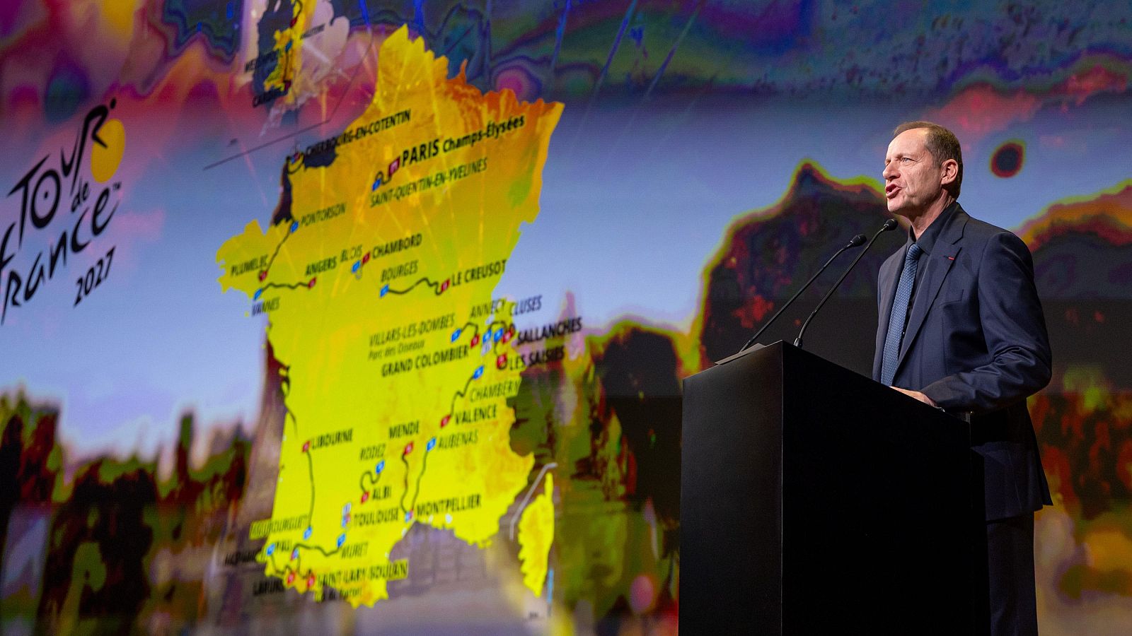 Christian Prudhomme habla ante un atril con un mapa gigante de Francia de fondo durante la presentación del Tour.