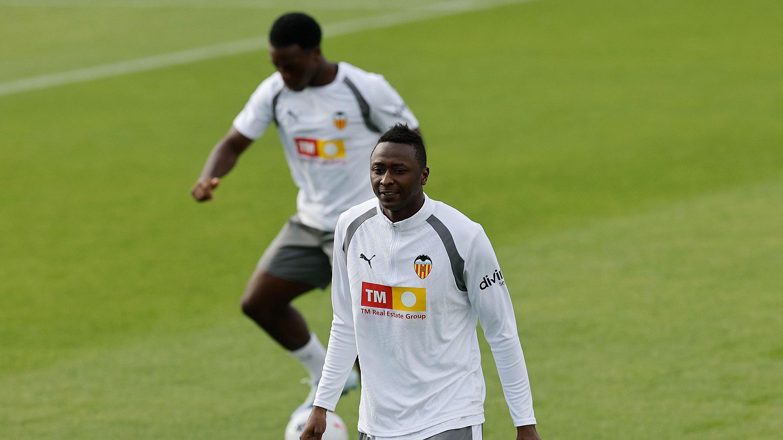 El defensa Mouctar Diakhaby camina de frente con sudadera blanca de entrenamiento, mientras Thierry Correia conduce un balón al fondo sobre césped natural.