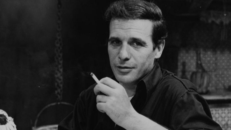 Retrato en blanco y negro del joven actor Paco Rabal mirando a cámara con expresión seria y un cigarrillo en la mano.