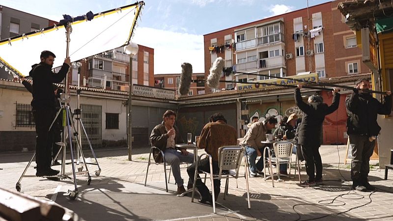Rodaje de una escena cinematográfica en una terraza urbana con actores y equipo técnico de iluminación y sonido.