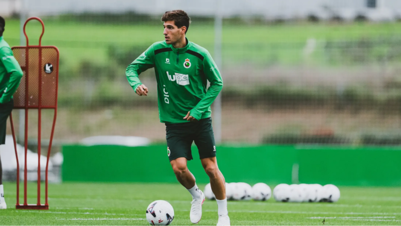 Futbolista del Racing de Santander conduce el balón durante un entrenamiento sobre césped natural con indumentaria oficial verde y equipamiento deportivo.
