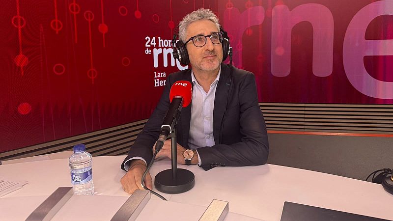 Arcadi España en el estudio de radio con auriculares y micrófono de RNE, ante un fondo acústico rojo con la rotulación del programa.