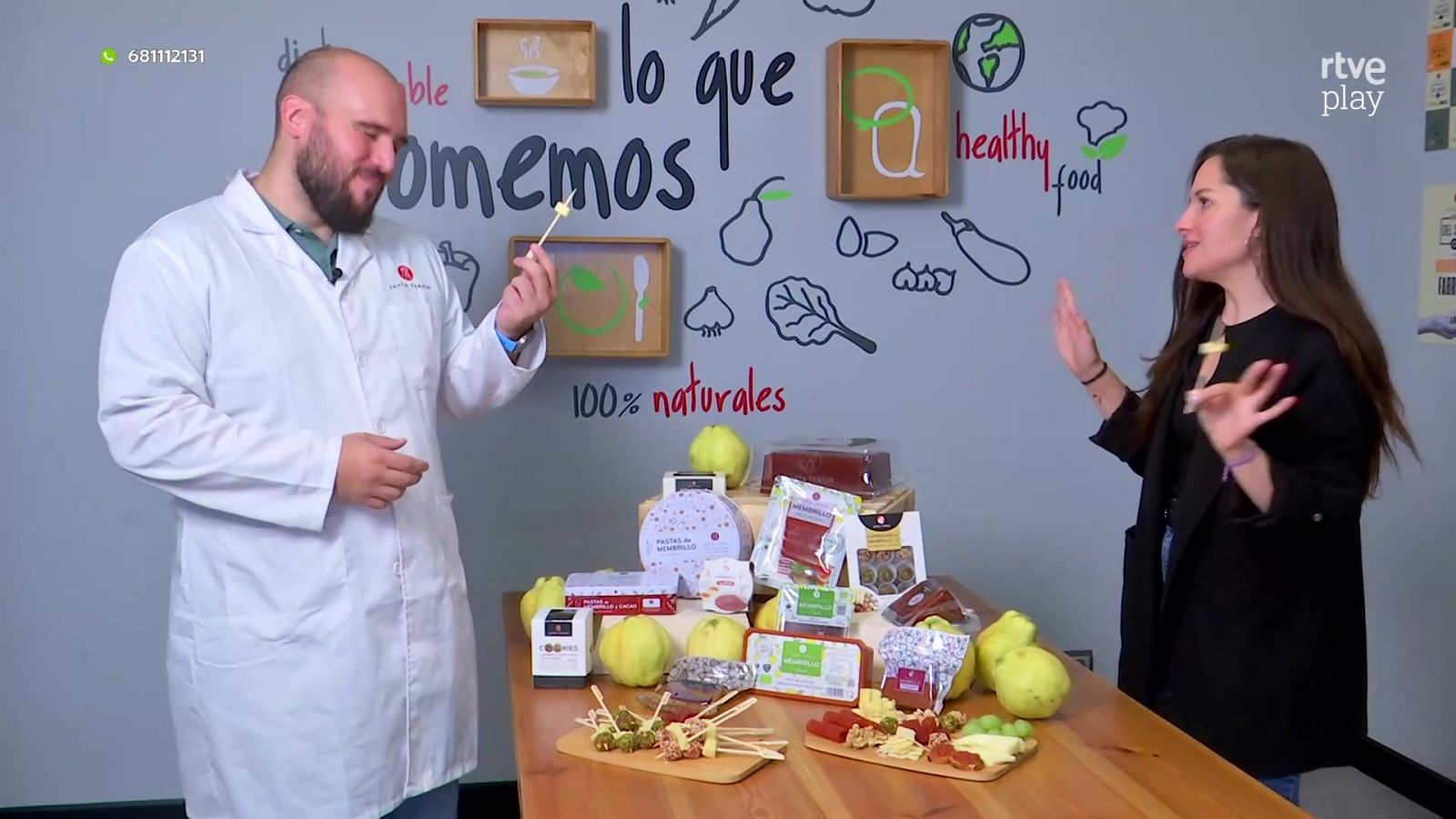 Dos personas presentan alimentos y aperitivos de membrillo en un plató con decoración temática sobre nutrición y salud.