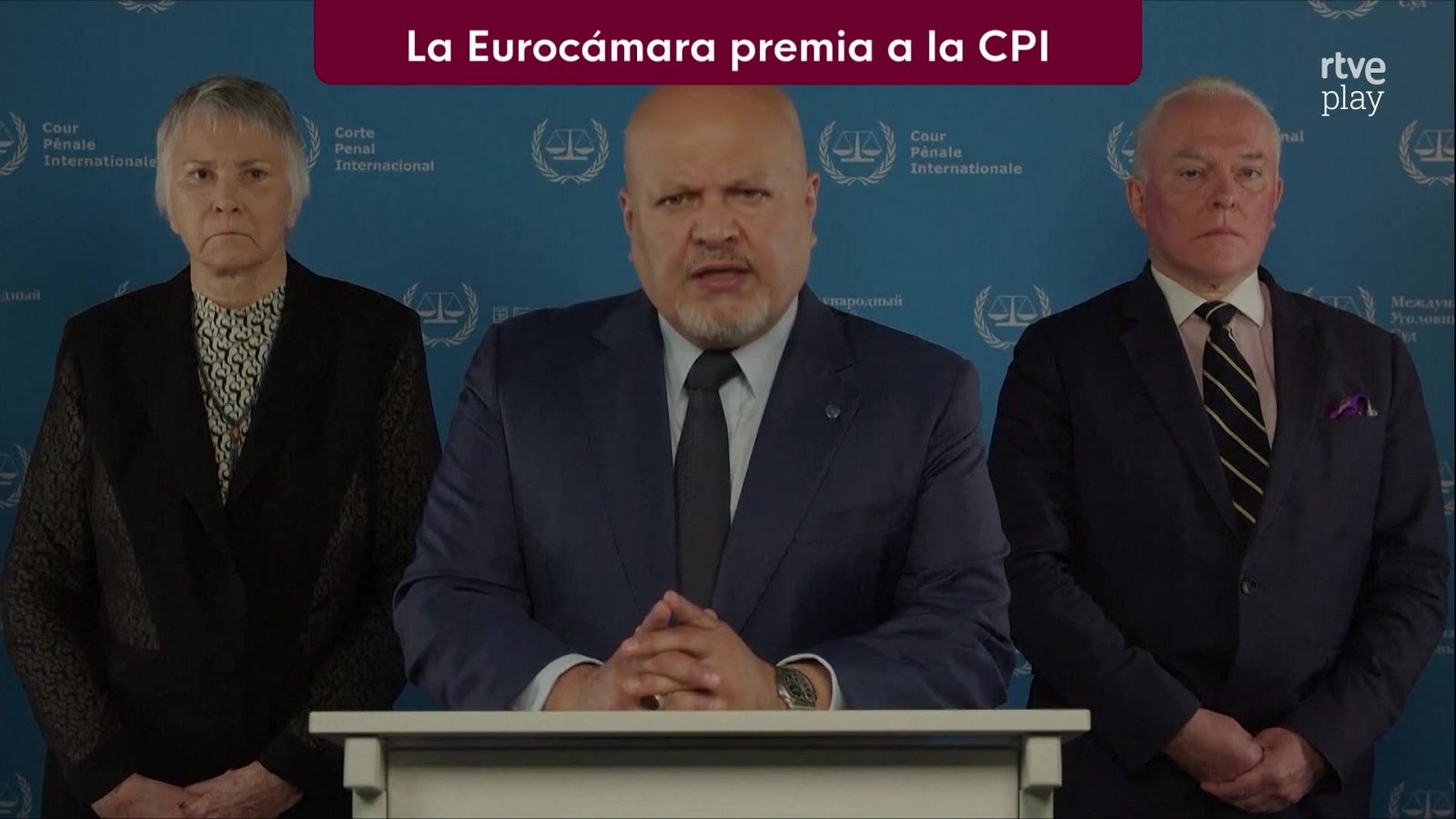 Tres miembros de la Corte Penal Internacional comparecen ante los medios frente a un panel azul corporativo.