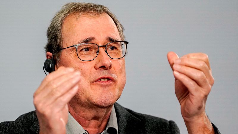 El biofísico Pascal Mayer habla con gesto expresivo, vistiendo americana gris y auricular en la oreja sobre fondo neutro.