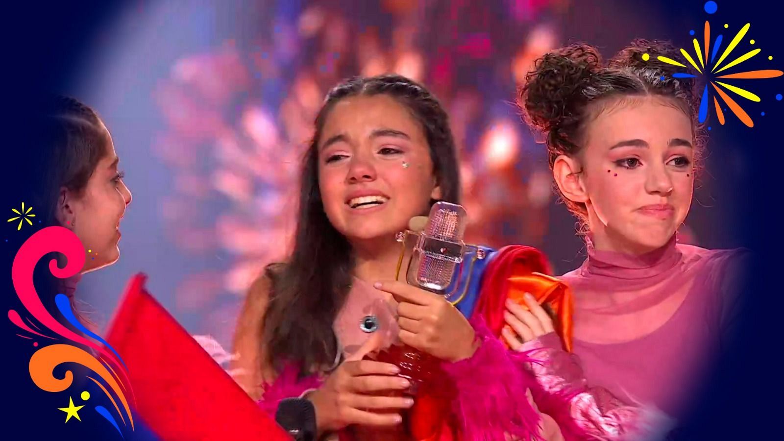 La cantante armenia Maléna celebra emocionada la victoria en Eurovisión Junior sosteniendo el trofeo de cristal, acompañada por su equipo en el escenario.