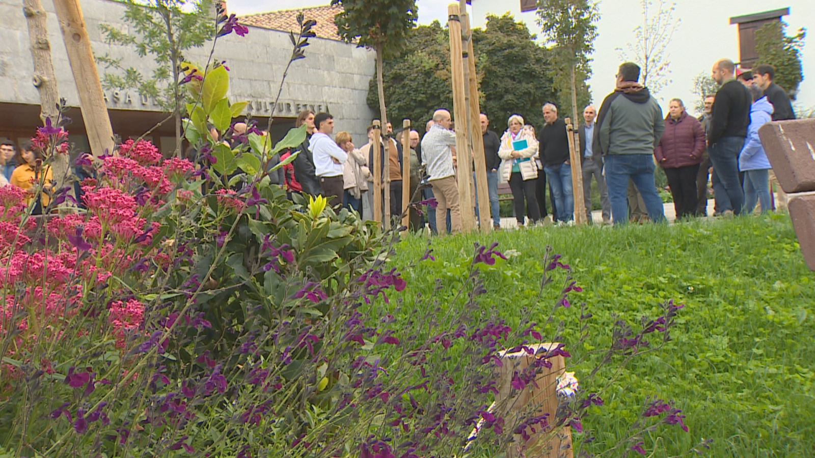 Grupo de personas asistiendo a un acto de plantación de árboles frente a un edificio con la inscripción bilingüe 'CASA DE CULTURA / KULTUR ETXEA'.
