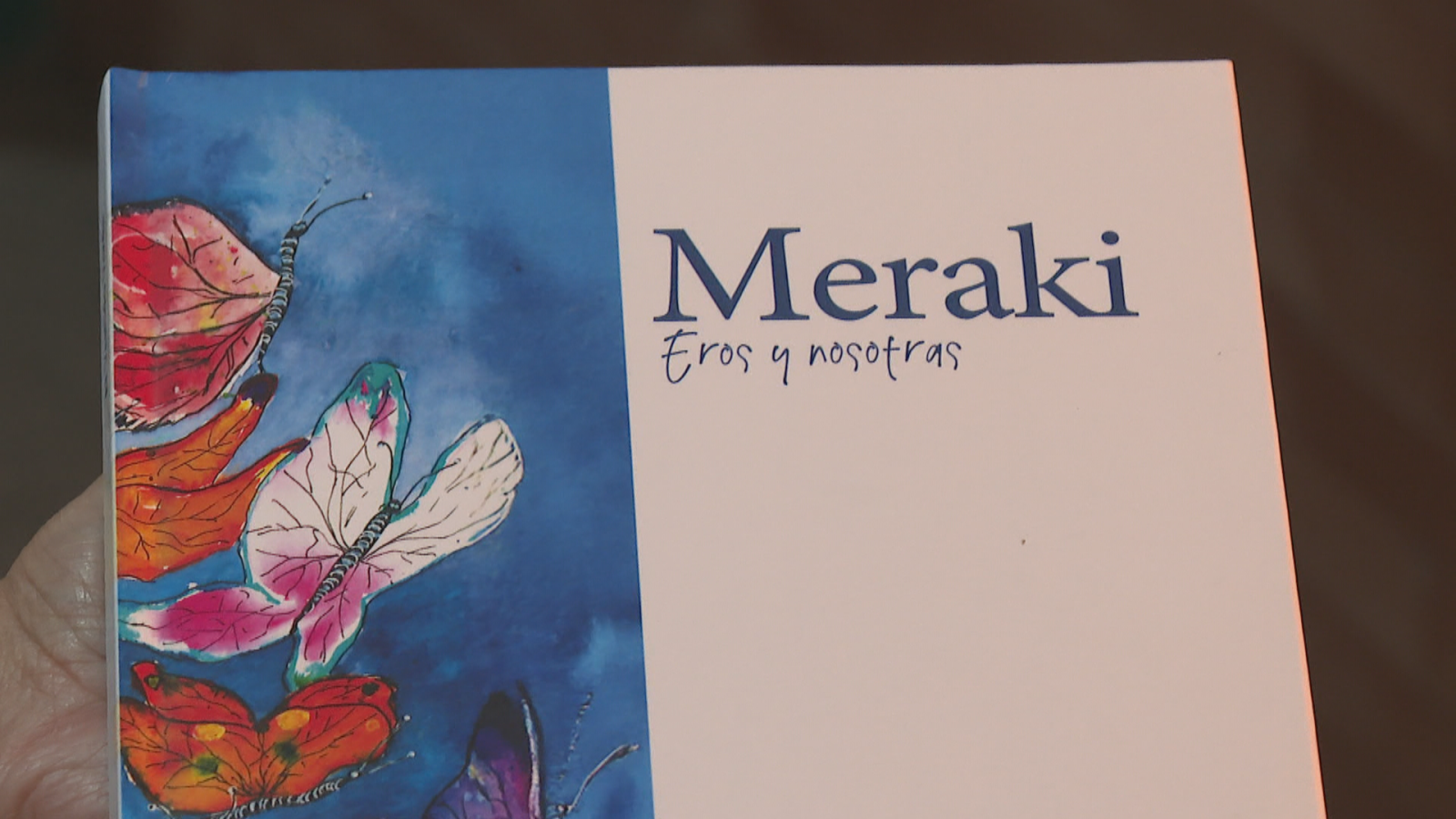 Portada de libro sostenida en la mano con diseño dividido entre ilustraciones de mariposas y el título impreso sobre fondo claro.