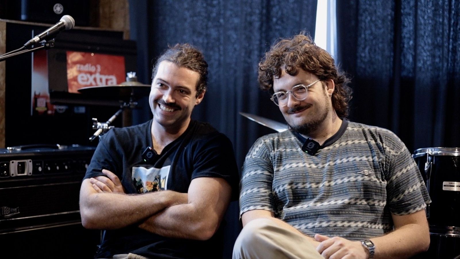 Joan Delgado y Aleix Turon, miembros del dúo Cala Vento, posan sonrientes en un set musical con instrumentos de fondo.