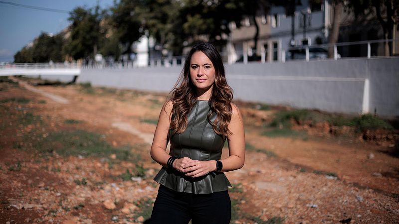 Mujer de pie en terreno árido luciendo top verde oliva, pantalones negros y mirada serena ante la cámara.