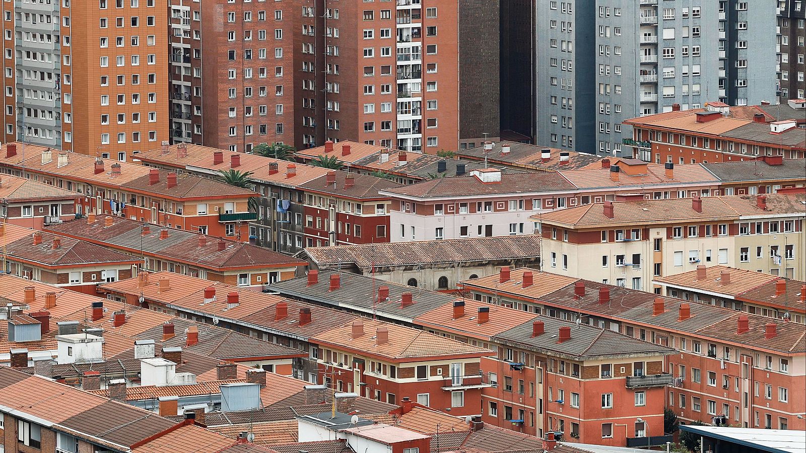 Vista panorámica urbana con edificios residenciales de baja altura y torres altas al fondo en una composición arquitectónica.