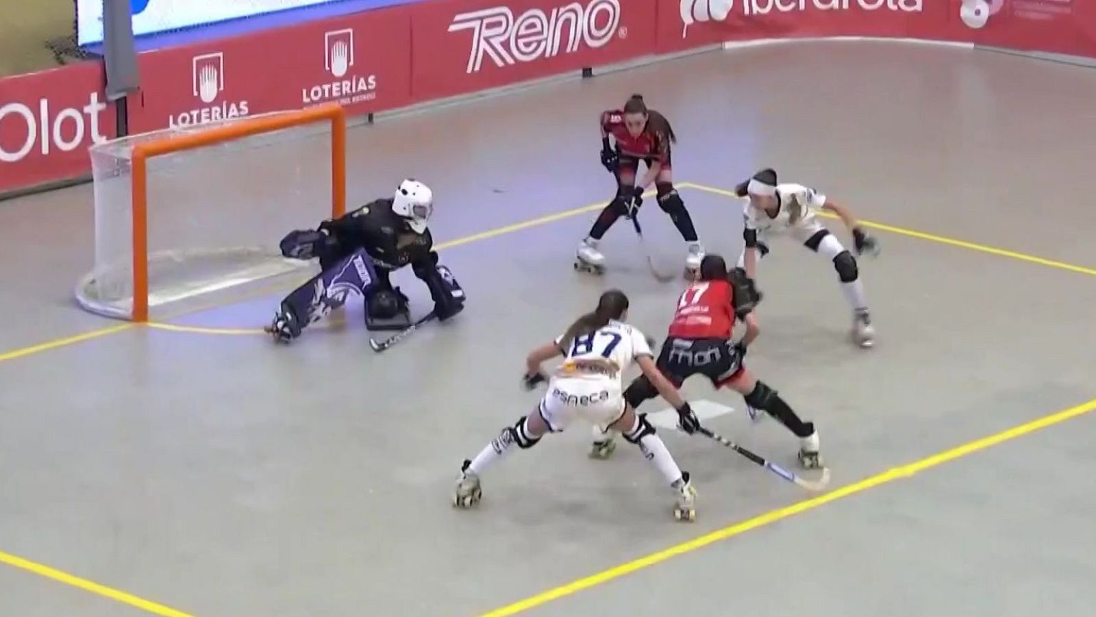 Intensa jugada en el área durante un partido de hockey sobre patines en pista cubierta con jugadoras disputando la bola.