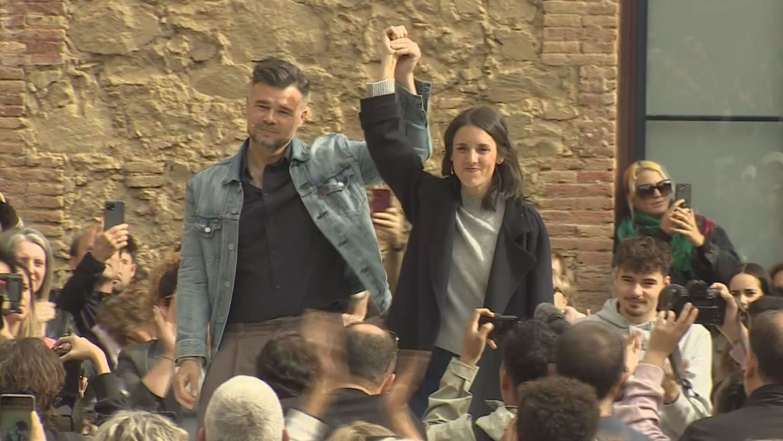 Gabriel Rufián e Irene Montero entrelazan sus manos en un acto público al aire libre ante una multitud que los observa.