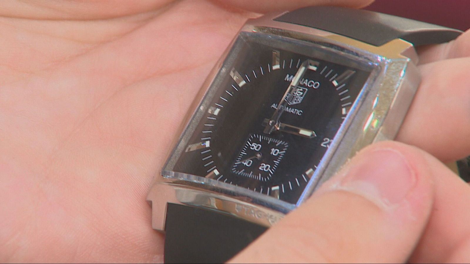 Primer plano de unas manos sosteniendo un reloj analógico de lujo con caja cuadrada, esfera negra y detalles plateados.