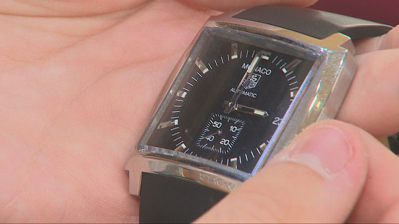 Primer plano de unas manos sosteniendo un reloj analógico de lujo con caja cuadrada, esfera negra y detalles plateados.