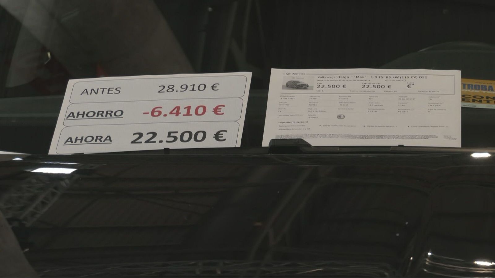 Detalle del parabrisas de un coche en exposición con un cartel de precios y una ficha técnica informativa.