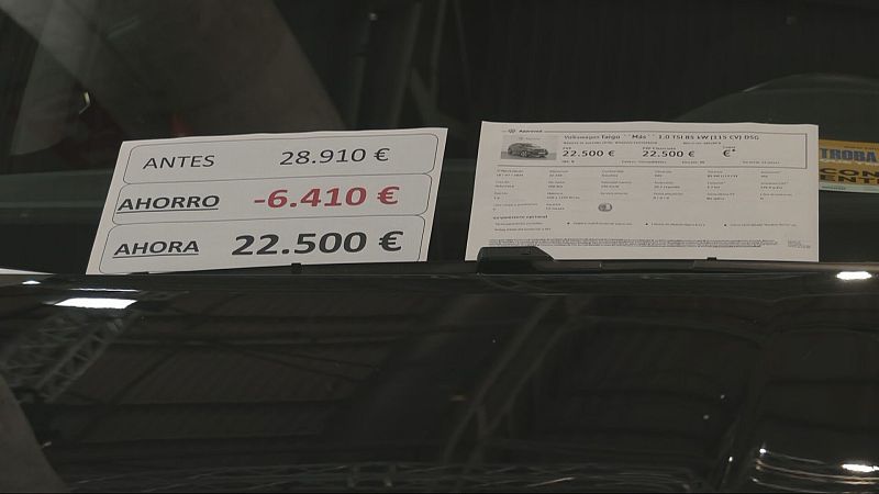 Detalle del parabrisas de un coche en exposición con un cartel de precios y una ficha técnica informativa.