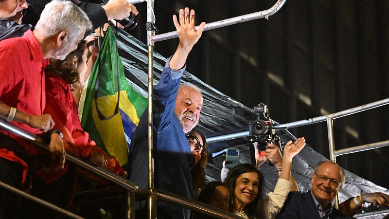 Luiz Inácio Lula da Silva y Geraldo Alckmin saludan sonrientes desde una plataforma elevada durante una celebración nocturna rodeados de simpatizantes y cámaras.