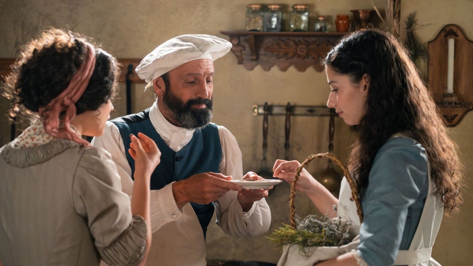 Tres sirvientes en una cocina rústica del siglo XVIII; el cocinero central muestra un plato a una criada mientras otra observa.