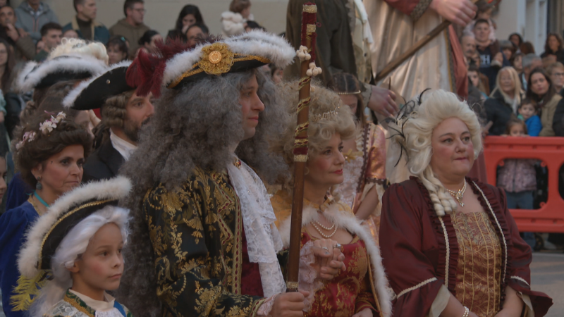 Recreación histórica barroca en la calle con participantes vestidos con trajes de época y pelucas, encabezados por un hombre que representa a Felipe V.