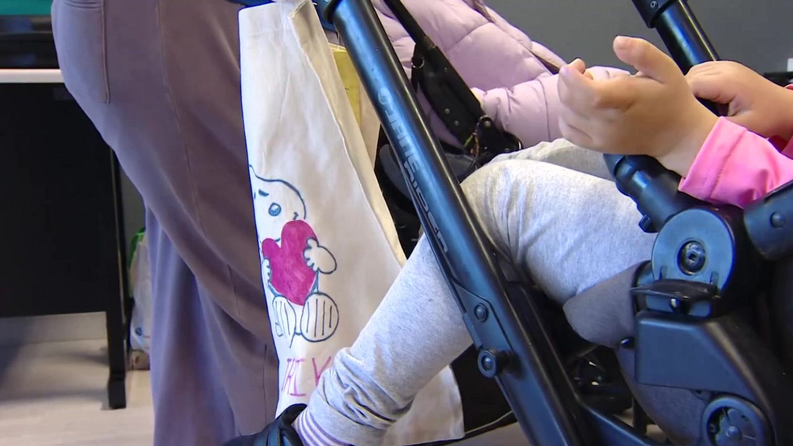 Plano detallado de un carrito infantil negro con un niño pequeño dentro, acompañado por adultos en un entorno interior.