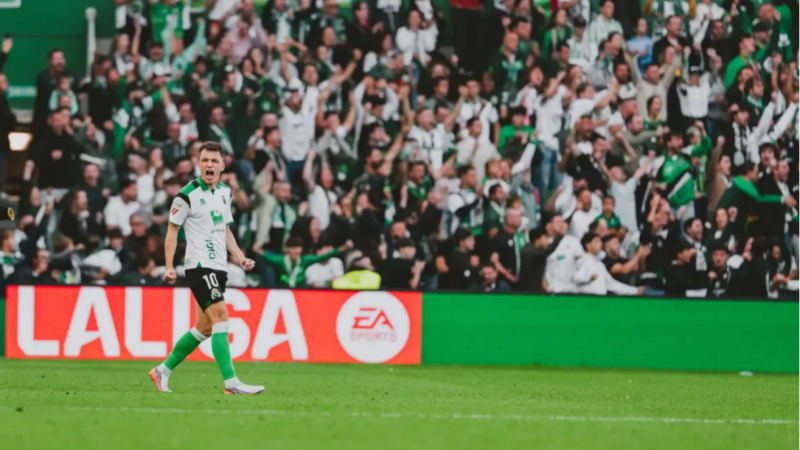 El futbolista Íñigo Vicente celebra con euforia en el campo de césped verde, vistiendo camiseta blanca y pantalón negro con el número 10, ante una grada llena de aficionados.