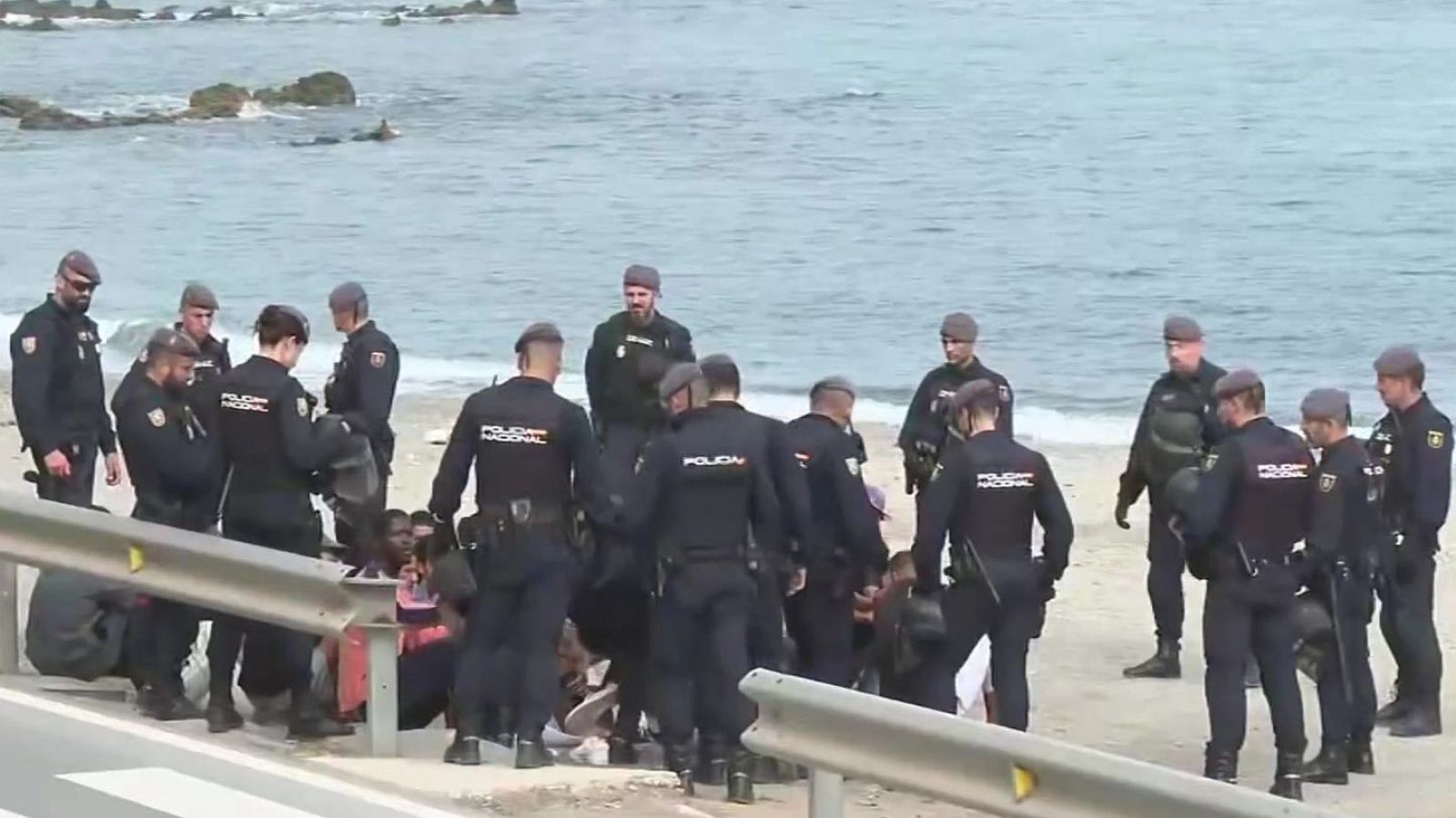 Agentes de la Policía Nacional custodian a un grupo de personas migrantes en una playa de Ceuta.