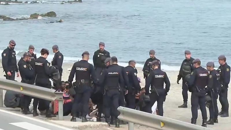 Agentes de la Policía Nacional custodian a un grupo de personas migrantes en una playa de Ceuta.