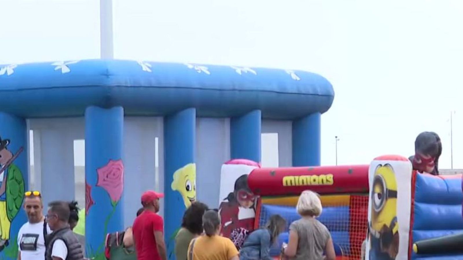 Zona de atracciones infantiles al aire libre con dos castillos hinchables decorados con personajes de animación y adultos supervisando.