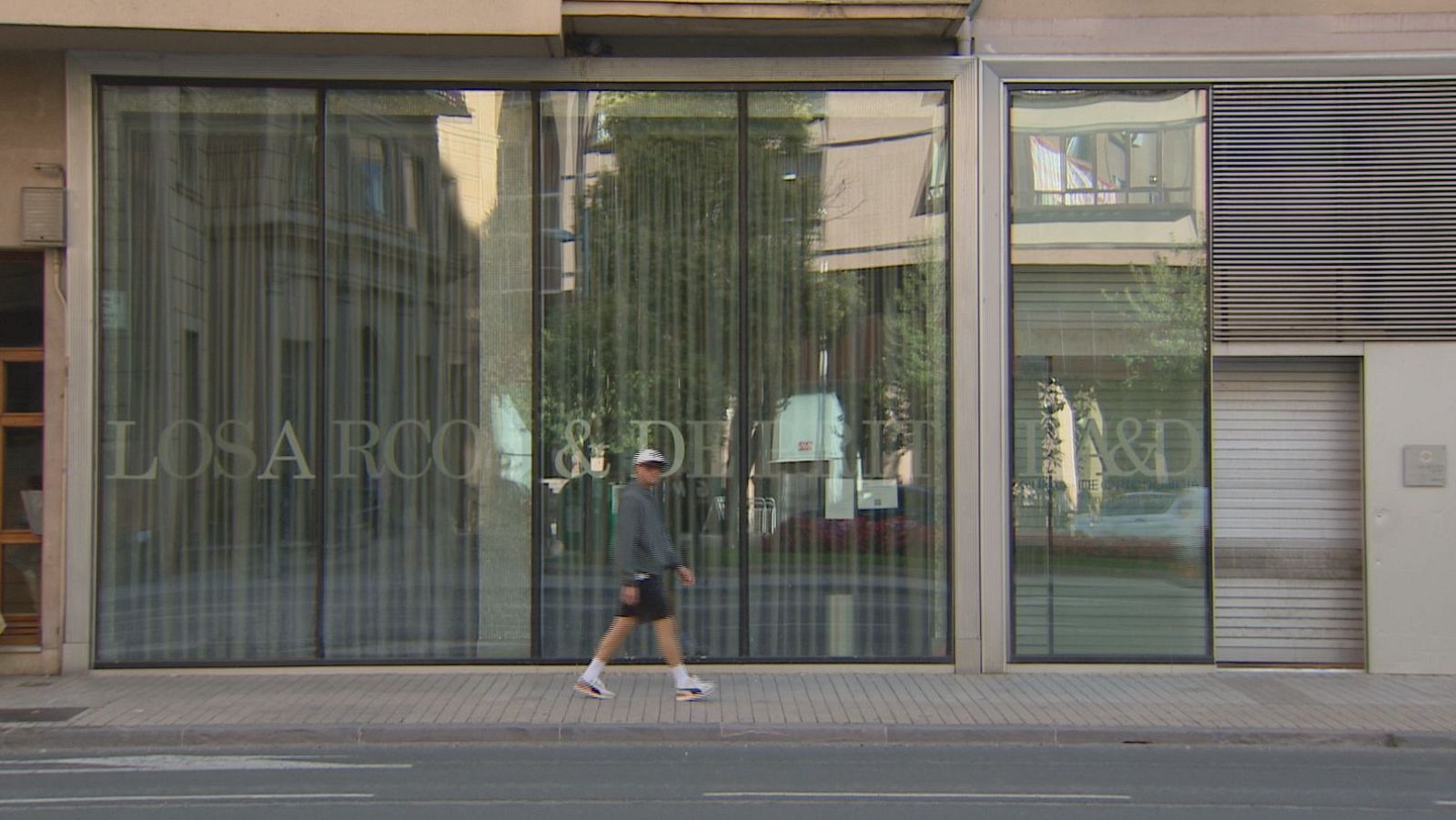 Fachada acristalada de una clínica dental en Pamplona con la inscripción «LOSARCOS & DE LA FUENTE» y un hombre con ropa deportiva caminando por la acera.