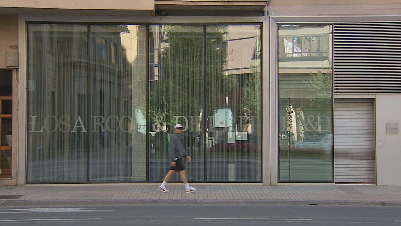 Fachada acristalada de una clínica dental en Pamplona con la inscripción «LOSARCOS & DE LA FUENTE» y un hombre con ropa deportiva caminando por la acera.