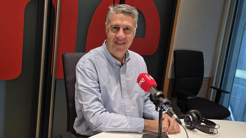 Plano medio de Xavier García Albiol sentado y sonriendo en un estudio de radio, frente a un micrófono con logotipo rojo y auriculares.