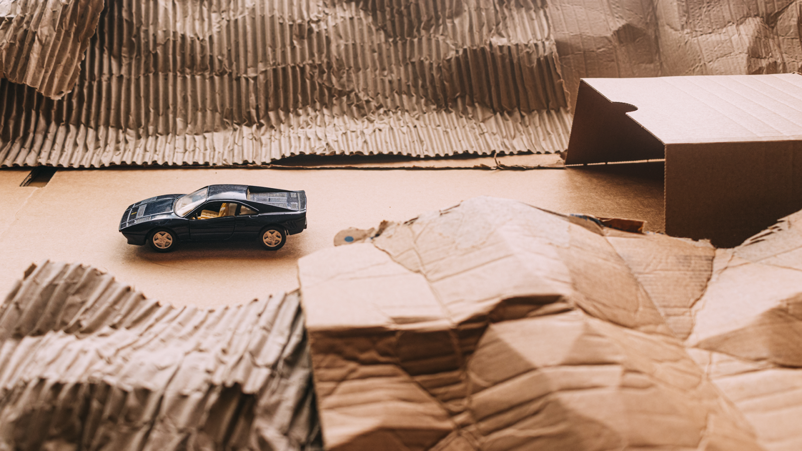 Diorama de paisaje montañoso y árido hecho de cartón con un coche deportivo clásico circulando hacia un túnel.