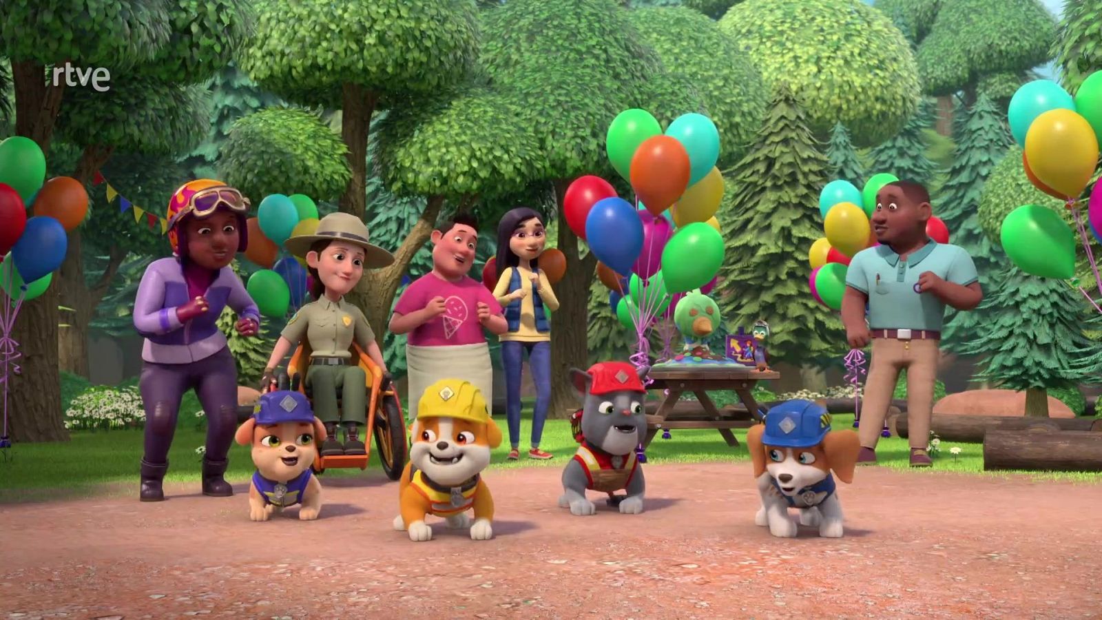 Cachorros constructores de la serie animada 'Equipo Rubble' posan alegres en un claro del bosque decorado con globos y una mesa de pícnic, rodeados por habitantes del pueblo.
