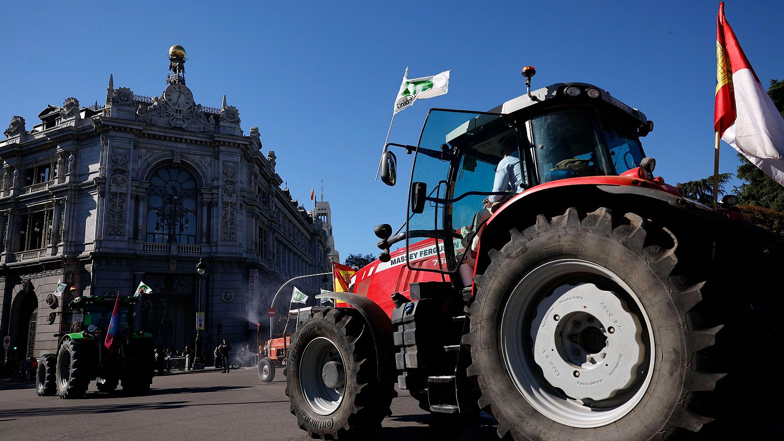 Tractor rojo Massey Ferguson circulando en protesta frente a la fachada del Banco de España en Madrid.