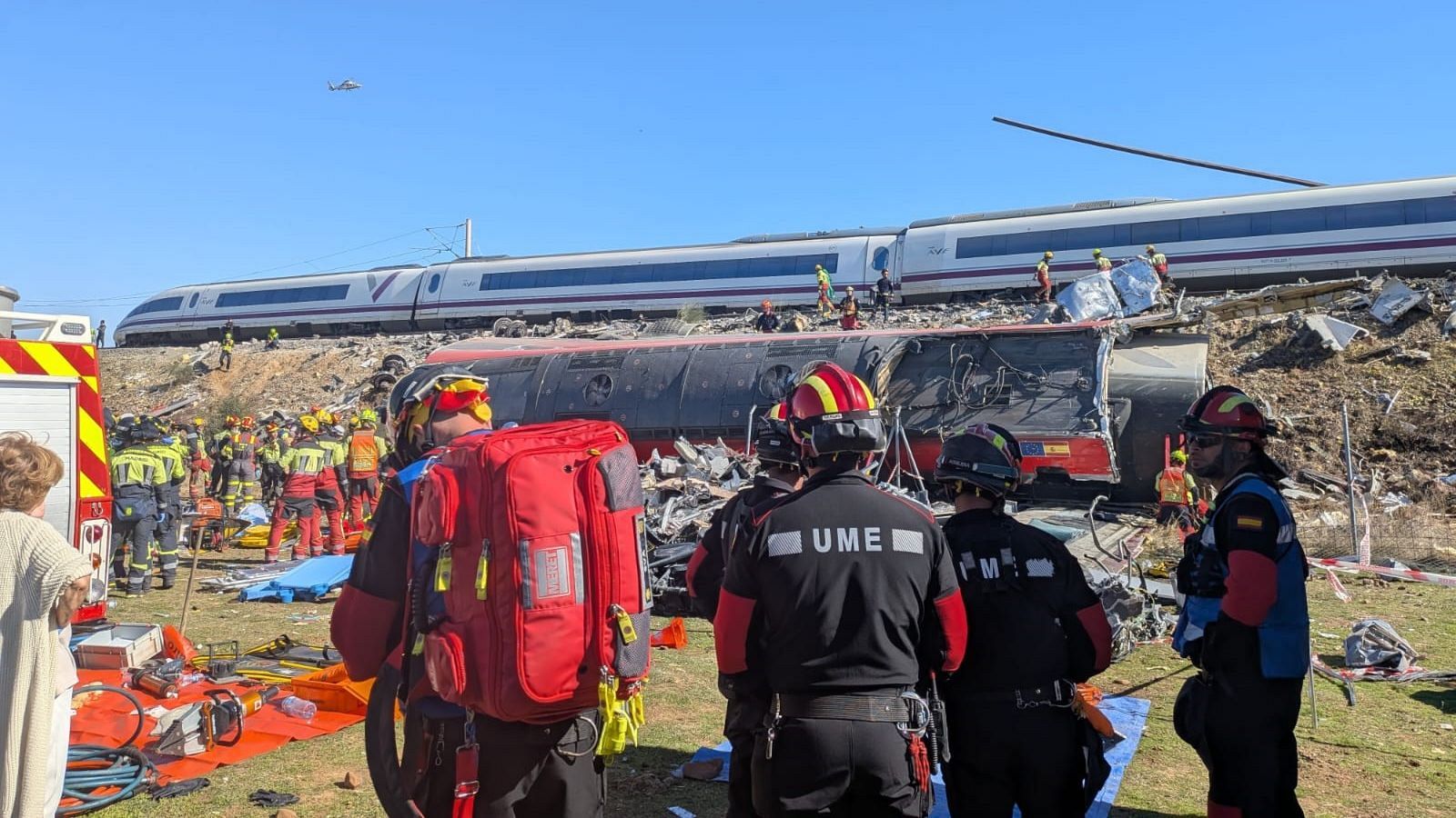 Efectivos de la UME y bomberos intervienen en el rescate de un accidente ferroviario con un vagón volcado y un tren de alta velocidad en las vías.