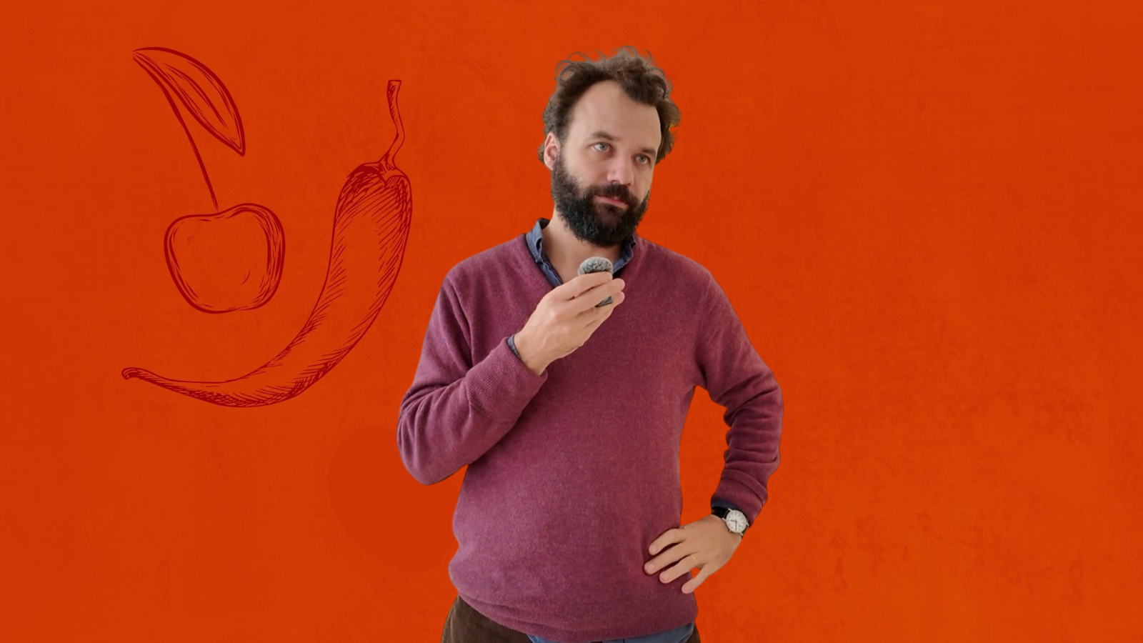 Hombre con barba y jersey granate sostiene un micrófono frente a un fondo rojo, acompañado de ilustraciones de una cereza y una guindilla.