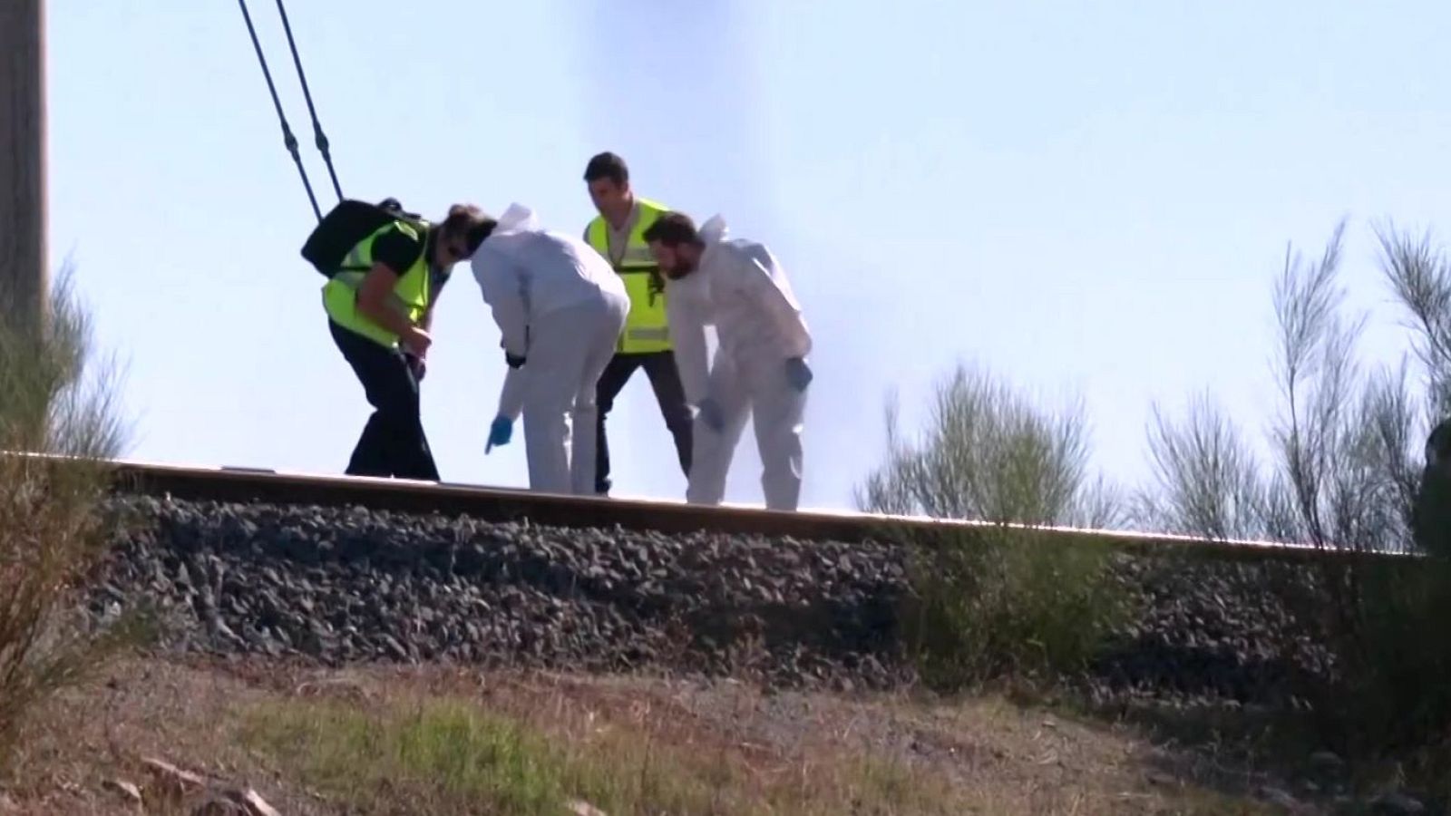 Técnicos e investigadores con monos blancos y chalecos reflectantes inspeccionan minuciosamente una vía de tren sobre balasto.