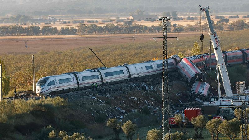 Imagen de un accidente ferroviario con un tren de Renfe descarrilado en un terraplén, donde operan una grúa pesada y operarios en una zona rural.