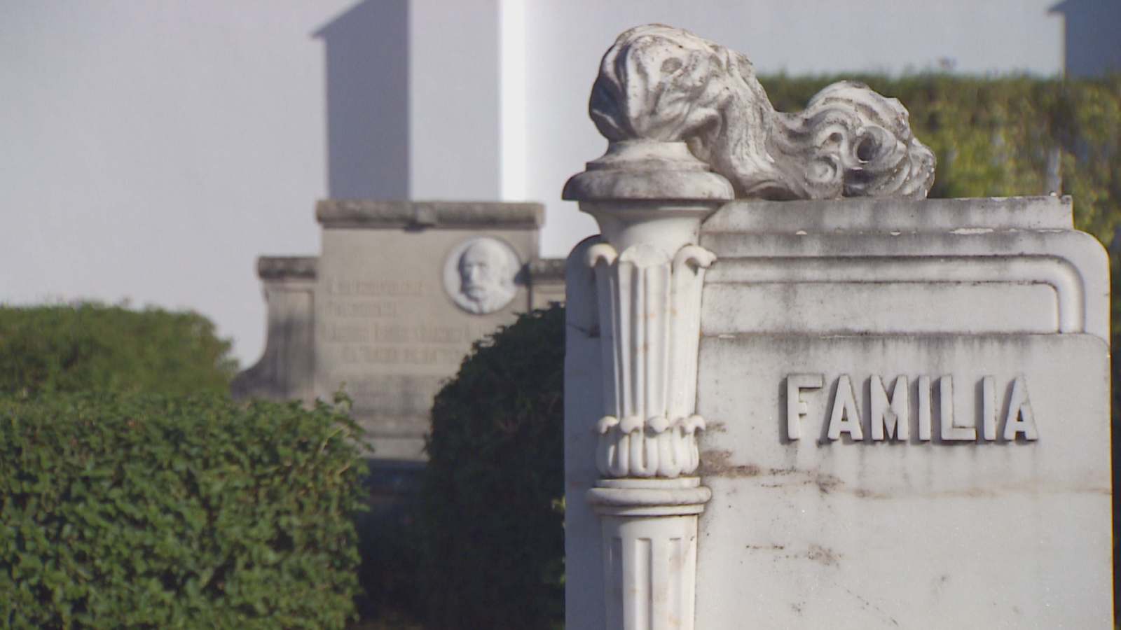 Monumentos funerarios en un cementerio con un panteón de mármol blanco que muestra la inscripción 'FAMILIA' y detalles esculpidos.