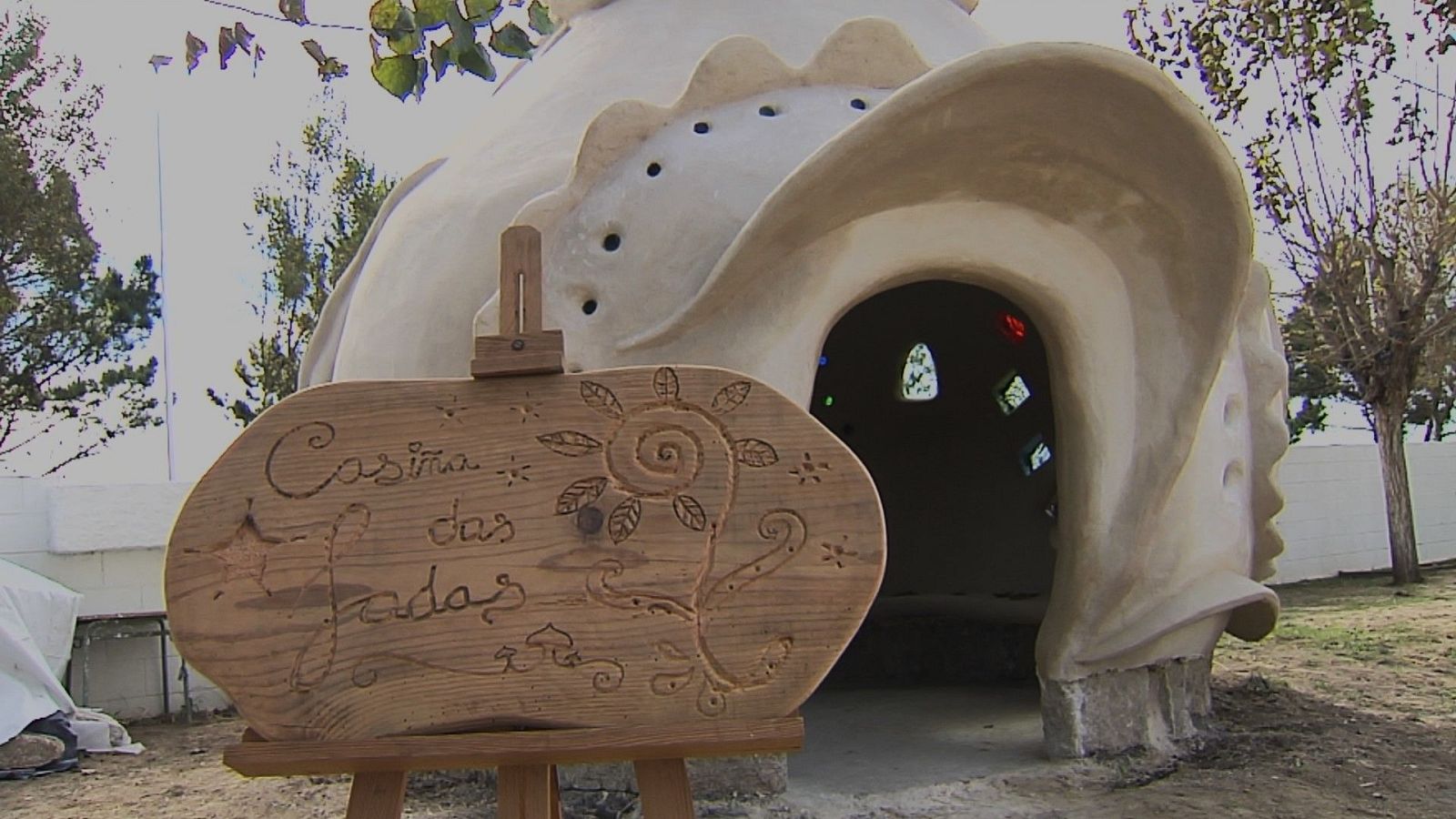 Cabaña artesanal de bioconstrucción en forma de cúpula con un cartel de madera en primer plano que reza «Casiña das fadas».