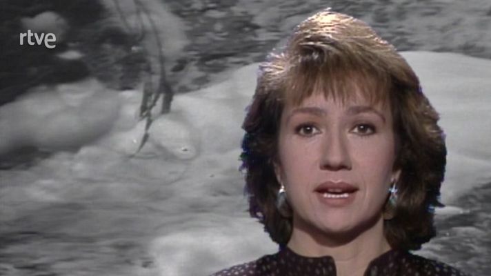 Primer plano de una presentadora con expresión seria, frente a un vídeo en blanco y negro de un río o masa de agua. Logotipo RTVE visible.
