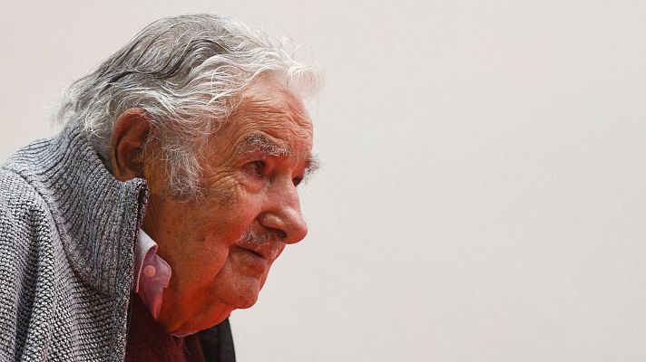 Primer plano de José Mujica de perfil, expresión serena, chaqueta gris sobre camisa burdeos, fondo claro.
