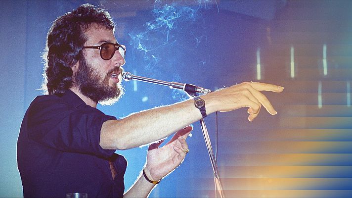Primer plano de Eugenio actuando, de perfil, con micrófono y cigarrillo encendido. Fondo de escenario desenfocado en tonos azules y púrpuras.