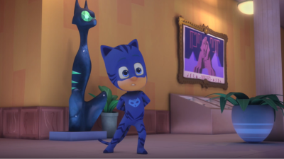 Catboy, el personaje de PJ Masks, se encuentra en un museo junto a una estatua felina y un cuadro con una esfinge. Detalle de plantas y una columna blanca.